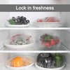 Various fresh foods like strawberries, oranges, and vegetables are stored in clear reusable cling film bags on a shelf.