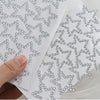 A hand is applying glitter gem stick-on facial tattoos onto a white surface.