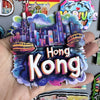 A hand holds a collection of wooden fridge magnets featuring a cityscape and the text Hong Kong.