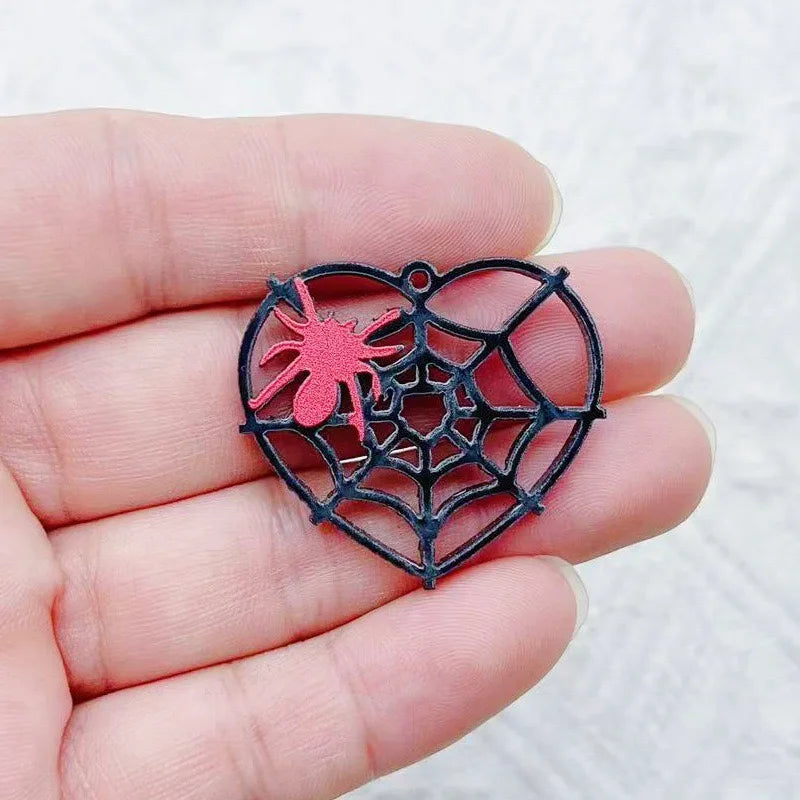 Una mano sostiene un colgante de Halloween de acrílico negro con un diseño de araña roja.