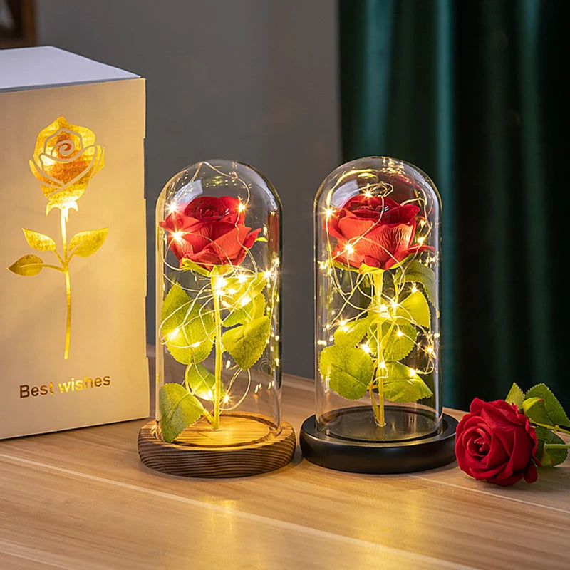 A glass dome candle featuring a red rose and green leaves, illuminated by warm LED lights.