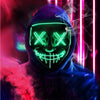 A person wearing a dark hoodie and a glowing green LED mask with an 'X' pattern, set against a background of red and pink lig