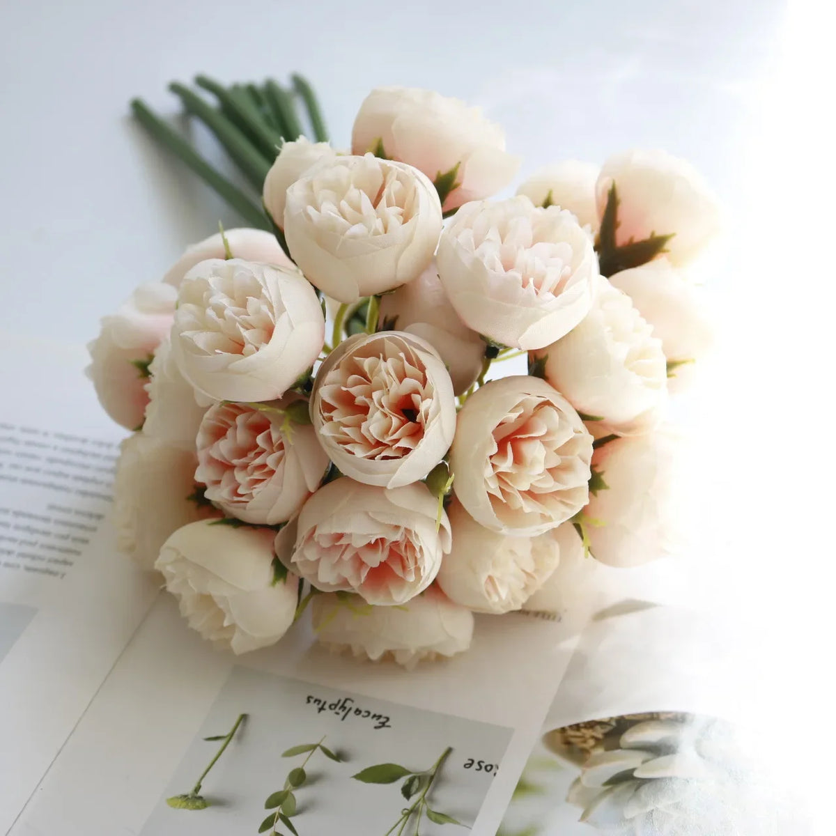 A bouquet of artificial pink peony silk flowers with green stems on a white background.