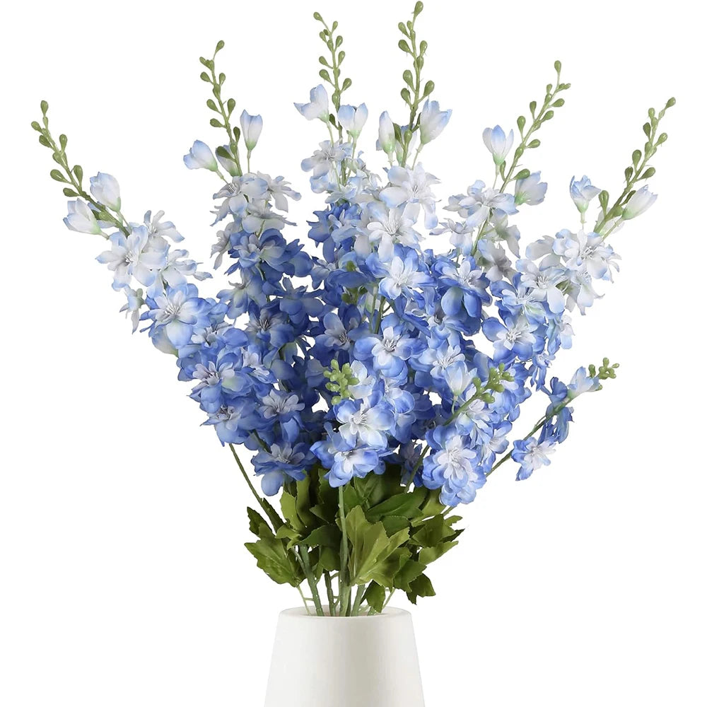 Un bouquet de fleurs artificielles de delphinium bleu et blanc dans un vase blanc.