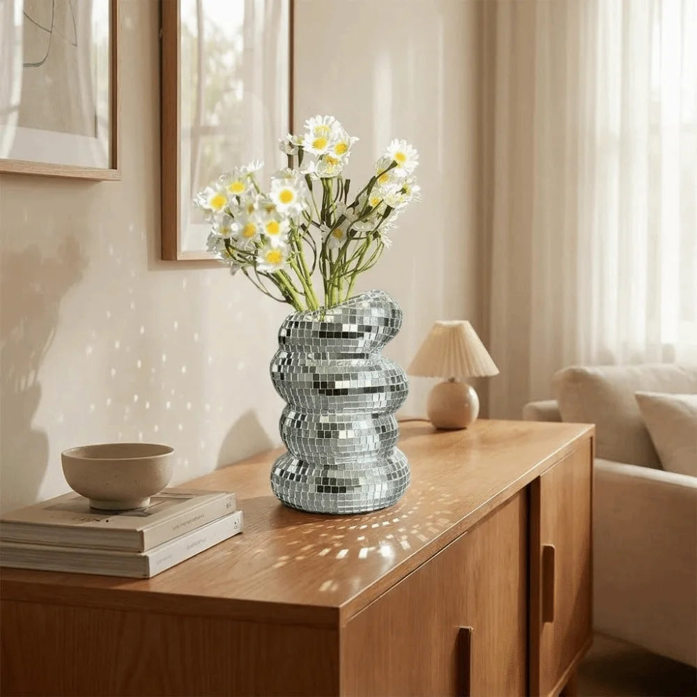 Silver disco ball spiral vase holding white daisies on a wooden cabinet top