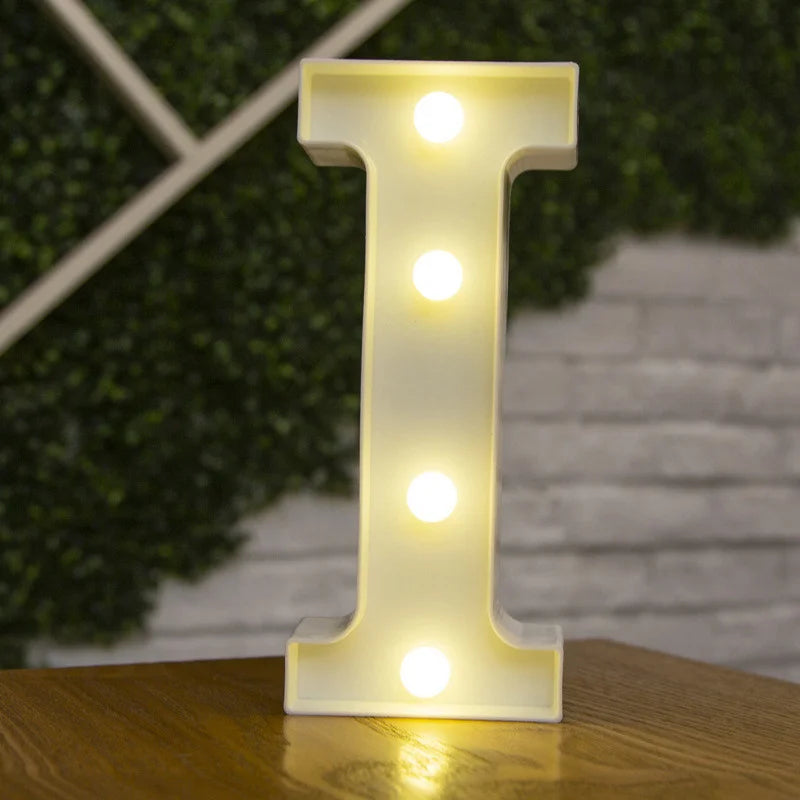 A glowing warm white LED alphabet letter light shaped like the letter I standing on a wooden surface.