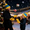 A man in a black suit and yellow gloves is smiling while a child wearing a blue beanie and yellow gloves laughs in a snowy ou