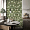 Espace salle à manger avec papier peint floral vert, meubles en bois et cuisine moderne.