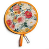 A round floral fabric fan with an orange rim and a tassel, featuring pink, yellow, and green flowers.