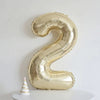 A large, gold foil number balloon shaped like the number 2, displayed on a white surface.
