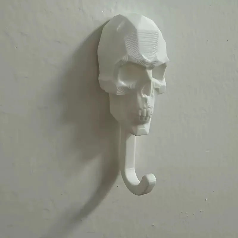 A white 3D skull wall hook with a curved hook, used for hanging items like towels or coats.