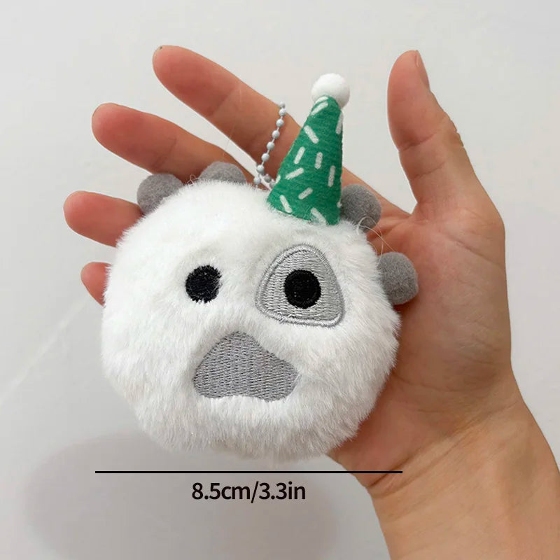 A white plush toy shaped like a bear face with gray ears and a green conical hat, held in a person's hand.