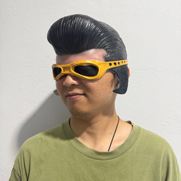 A man wearing a yellow half-face latex mask with dark hair and a green shirt.