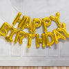 A golden foil letter balloon banner spelling out Happy Birthday hanging against a white wall.