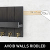 A hand is using a tool to mark a wooden piece, which is being placed onto a dark wood wall organizer with five brass hooks.