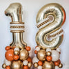 Two large gold foil number balloons, 1 and 8, decorated with tissue paper balls.