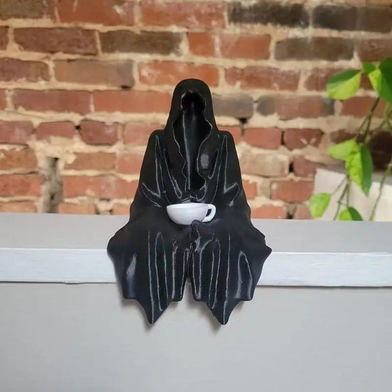 Black resin statue of a ghost figure holding a white teacup against a brick background.