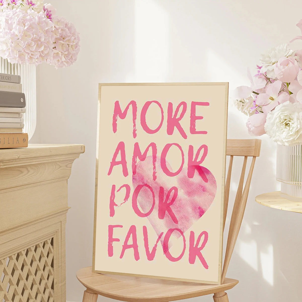 A framed canvas print featuring the pink watercolor text MORE AMOR POR FAVOR on a light background.