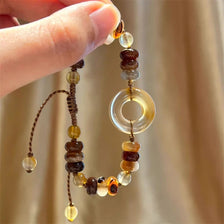 Hand holding a handmade red rope amulet bracelet with various colored beads and a clear disc charm