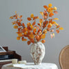 An arrangement of orange and yellow autumn beech leaves in a white ceramic vase on a table.