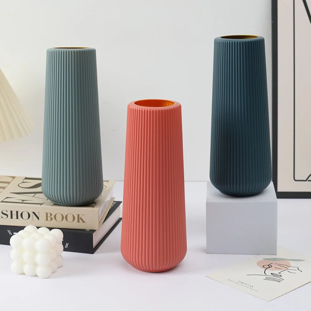 Three modern plastic flower vases in shades of sage green and coral standing on a white surface.
