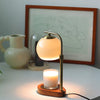 A brass aromatherapy wax melting lamp with a glowing orb and a lit candle sits on a white table.