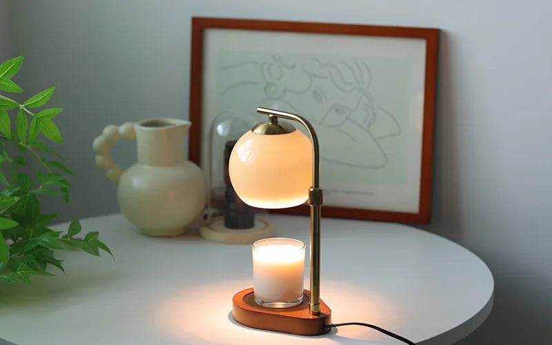 A brass aromatherapy wax melting lamp with a glowing orb and a lit candle sits on a white table.