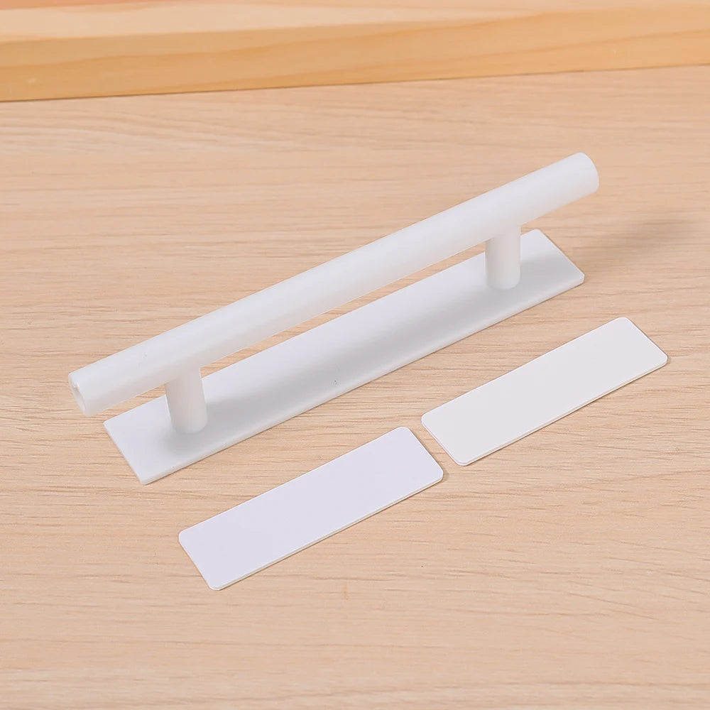 White self-adhesive cabinet handles or no-drill pulls for drawers and wardrobes shown on a wooden surface.