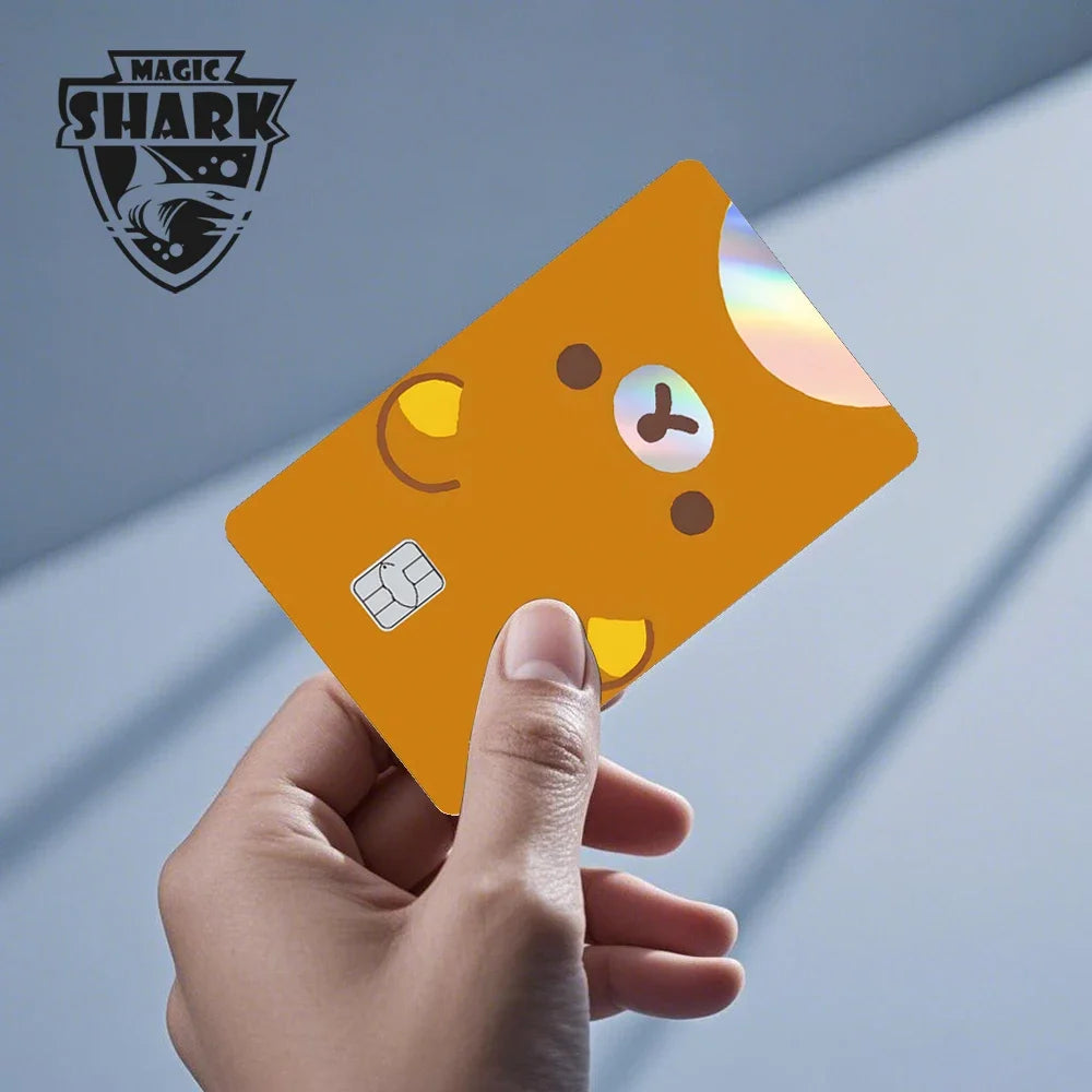 A hand holds a holographic cat credit card skin sticker with various icons against a light gray background.