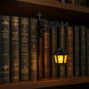 A vintage bookshelf lantern lamp with a wrought iron bracket illuminates a row of old leather-bound books.