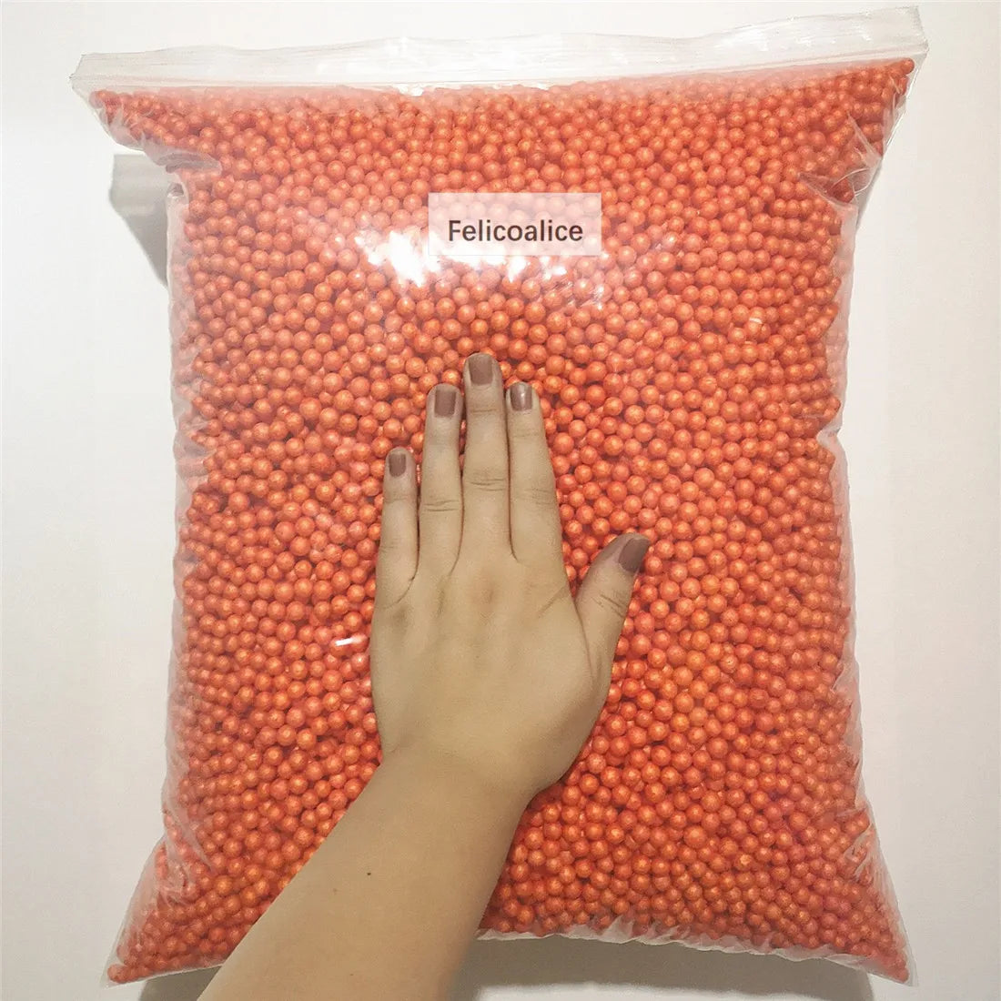 A hand is holding a clear bag filled with orange foam beads labeled Felicoalice.