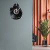 A black vinyl record wall clock with a white face and black markings is mounted on a gray wall.