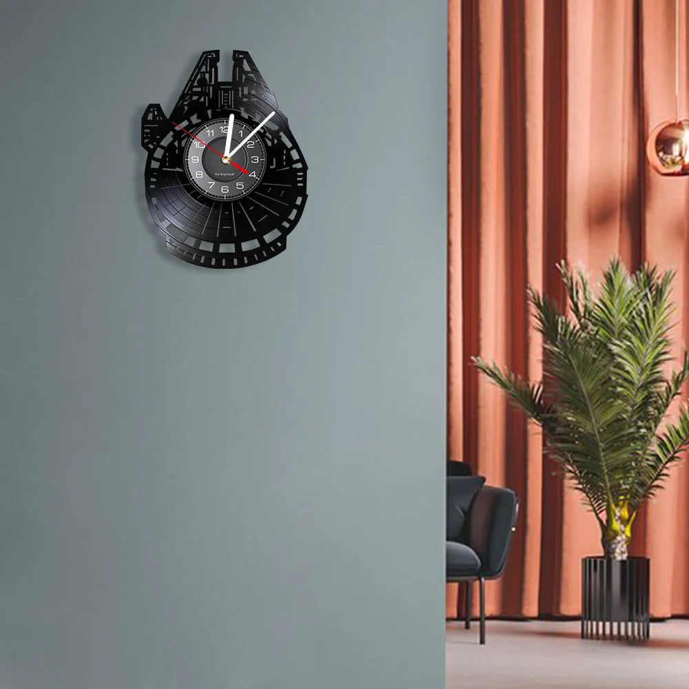 A black vinyl record wall clock with a white face and black markings is mounted on a gray wall.