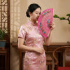 A woman in a pink silk dress holds a vibrant pink folding fan against a light background.