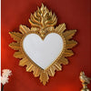 Ornate gold-framed heart-shaped wall mirror with flame detailing mounted on a red wall.