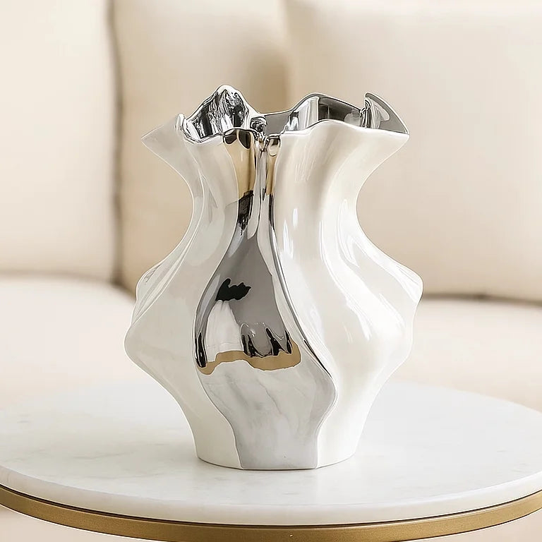 A white ceramic vase with a textured wave pattern and metallic accents sits on a round marble coaster.