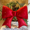 A large, shiny red satin bow balloon weight with pearl accents displayed on a table.
