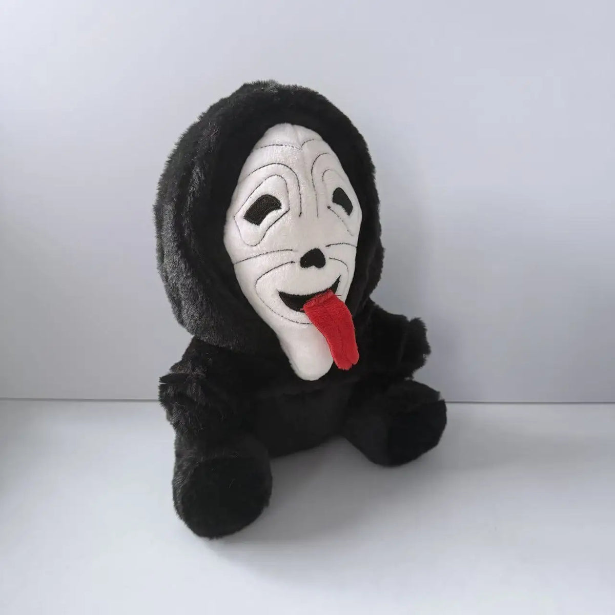 A black plush toy of Ghost Face with a white mask and a red tongue.