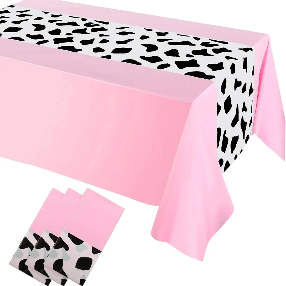 Pink cow print western tablecloth with black and white spots displayed on a table.