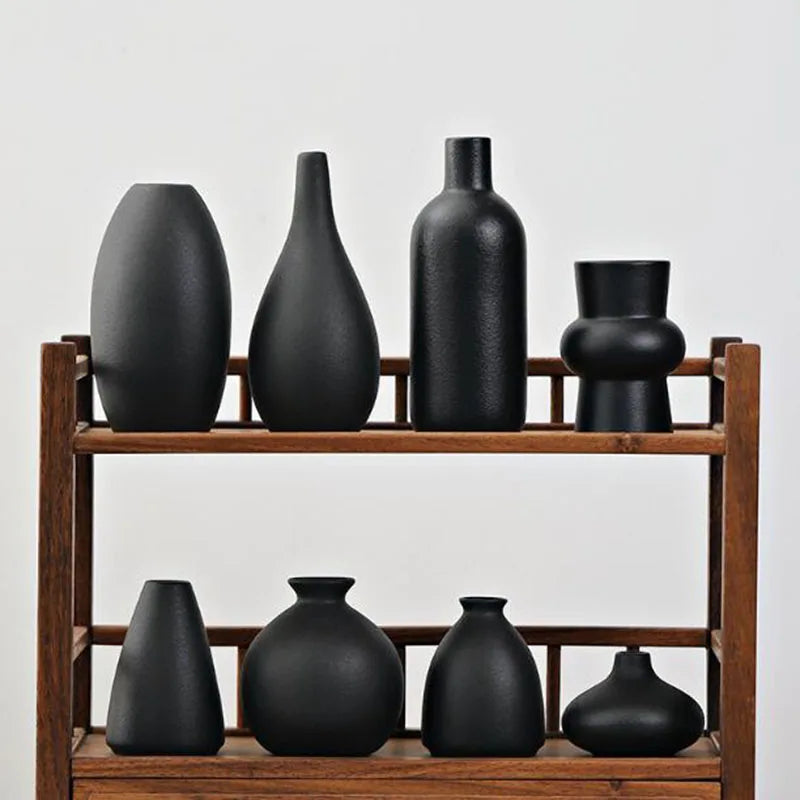 A set of five matte black ceramic vases displayed on a wooden shelf.