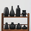 A row of modern ceramic vases in matte black displayed on a wooden shelf.