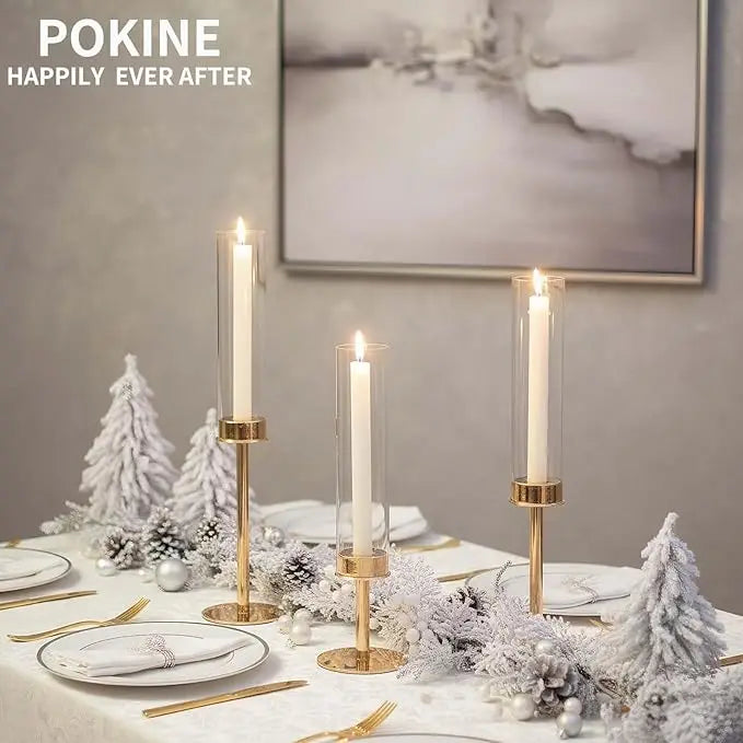 Three gold and silver hurricane candle holders decorated with white floral and winter greenery