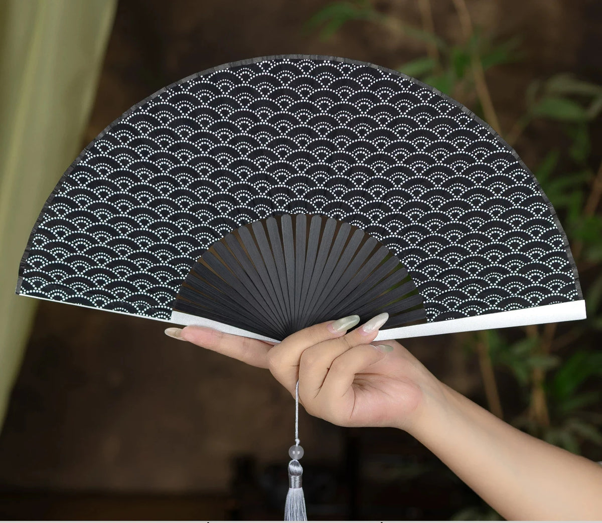 A hand is holding a black and white patterned folding hand fan with pleated ribs.