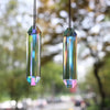 A pair of iridescent crystal pendants hanging against a blurred outdoor background.