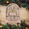 A pink wooden library shelf filled with books, set against a backdrop of green pine branches and pine cones.