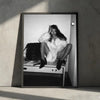 A black and white portrait of a model with long hair wearing a fluffy white coat sitting on a table.