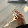 A hand holds a clear vintage French-style high-footed wine glass with intricate cut patterns.
