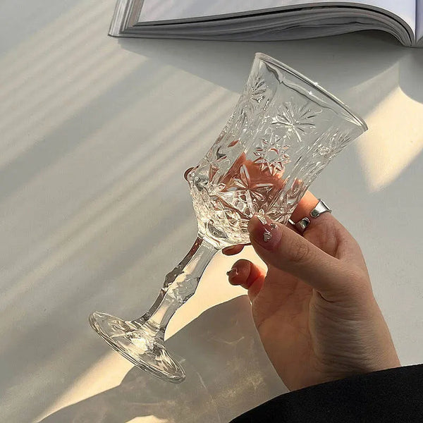 A hand holds a clear vintage French-style high-footed wine glass with intricate cut patterns.