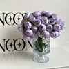 A bouquet of purple silk peonies in a glass vase displayed in front of a black and white logo box.