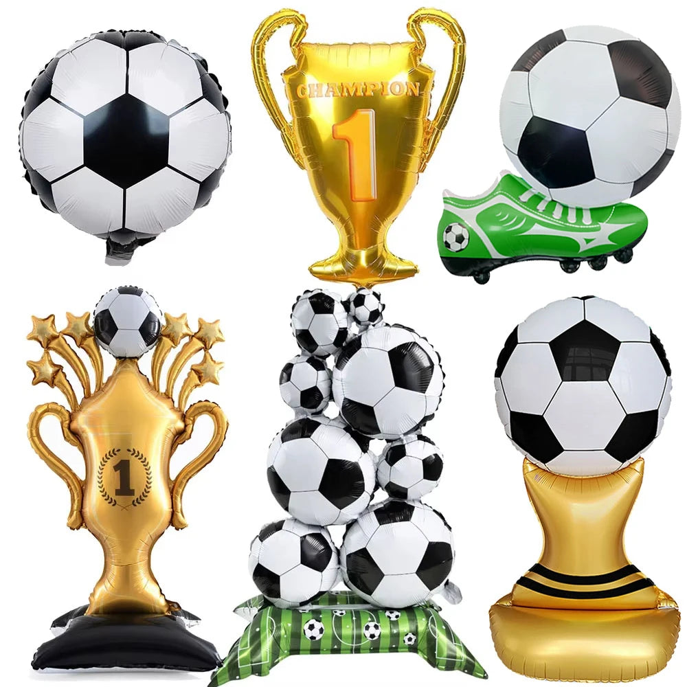 A collection of gold and black soccer-themed party décor including a trophy, a soccer ball, and a green and black soccer shoe